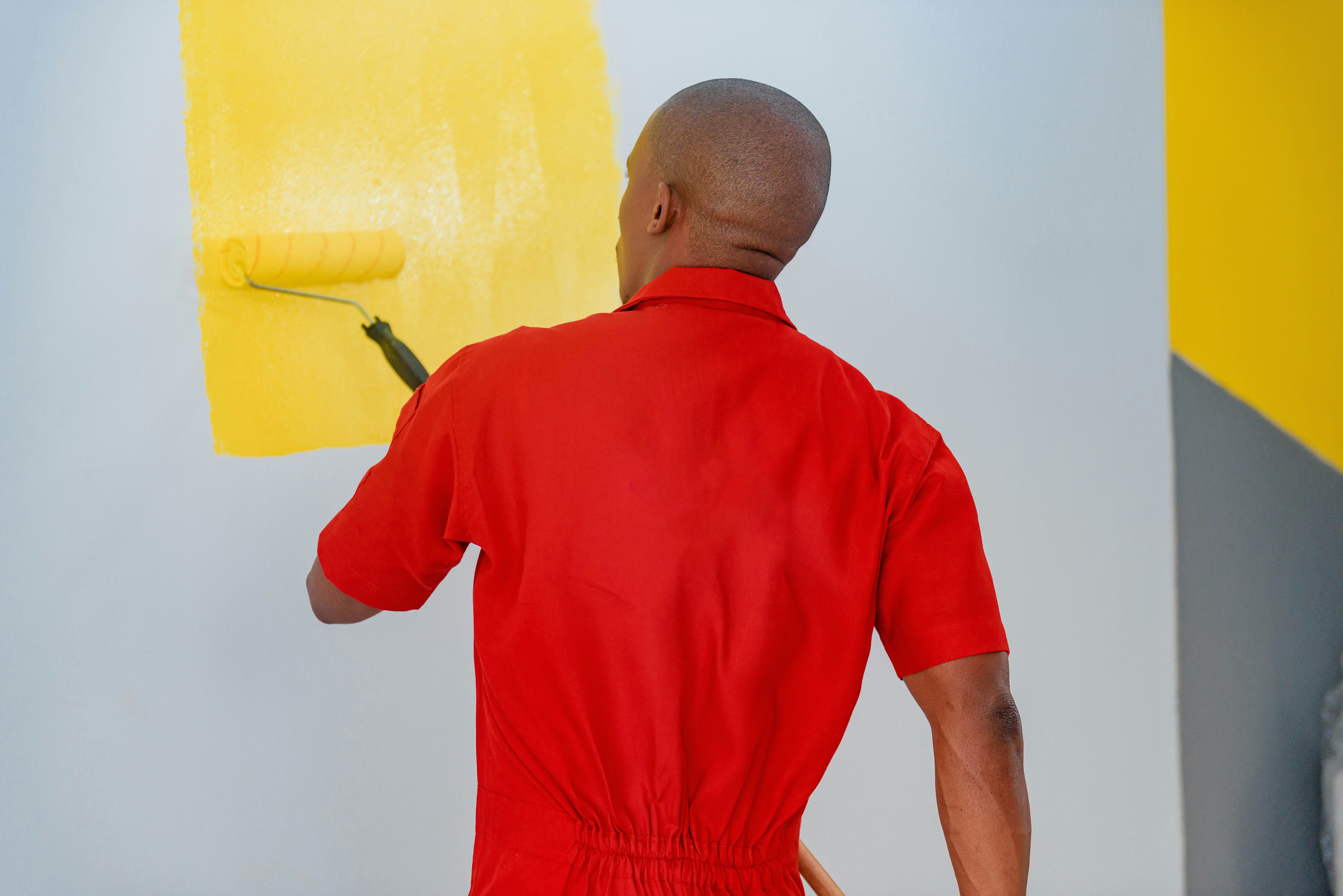 Solo tradesperson painting a wall, seen from behind mid-roll